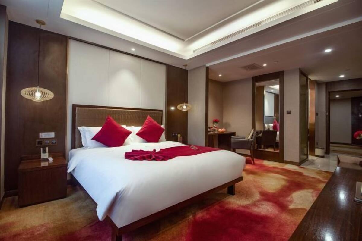 A hotel room with a large bed, a wooden nightstand, a desk, and a mirror.