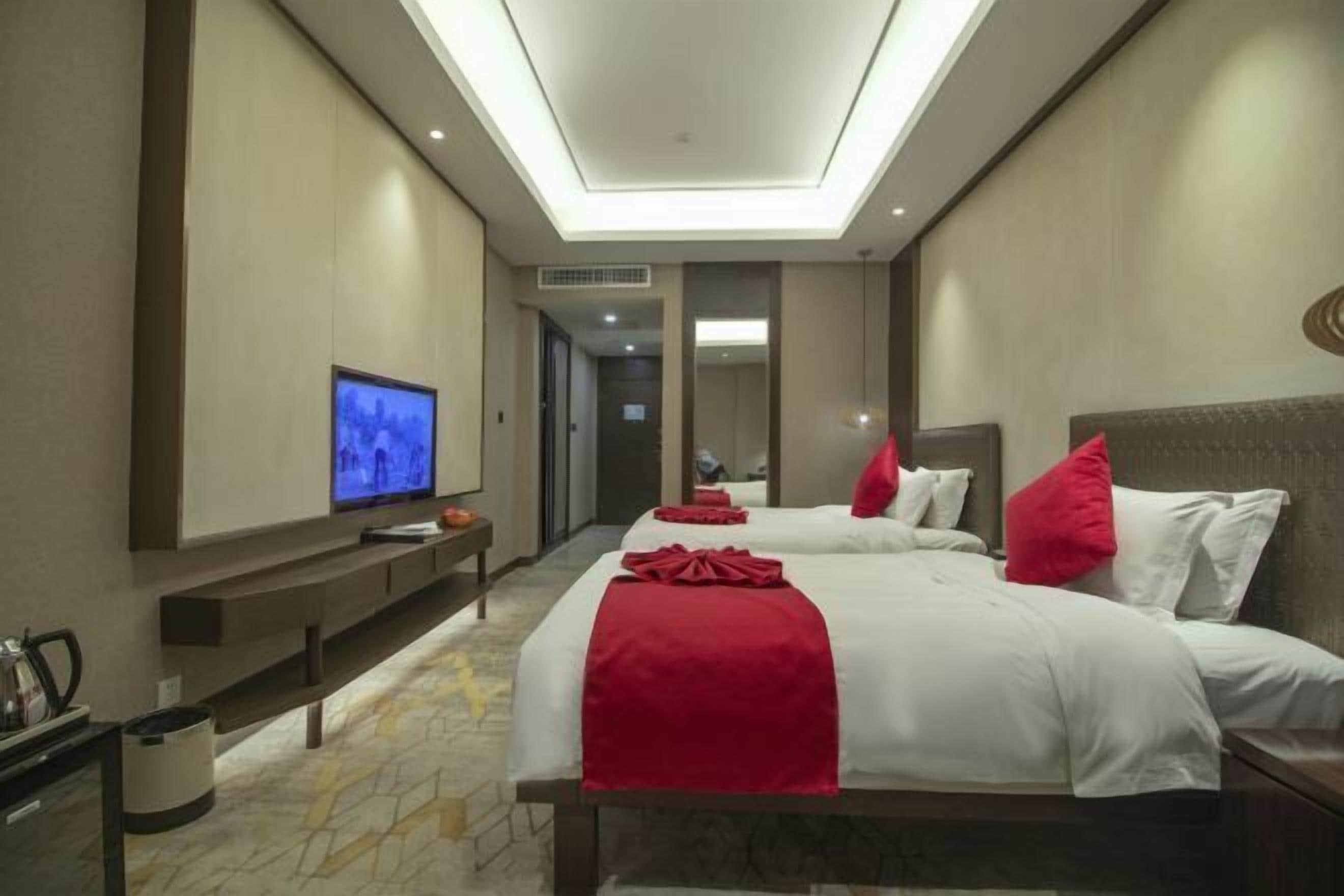 A hotel room with a large bed, a TV, a desk, and a mirror.