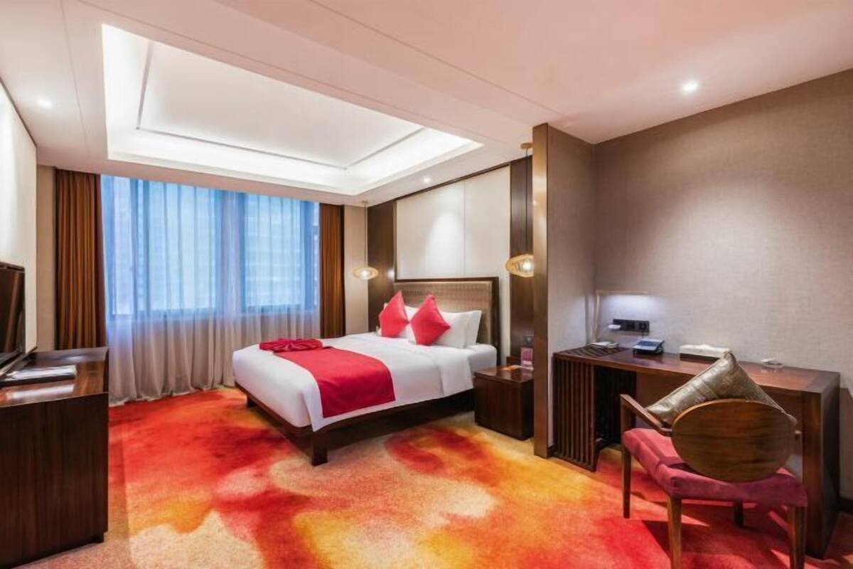 A hotel room with a large bed, a desk, a chair, and a TV.