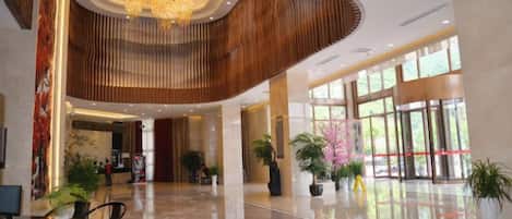 A spacious lobby with a curved wooden ceiling, a reception desk, and potted plants.