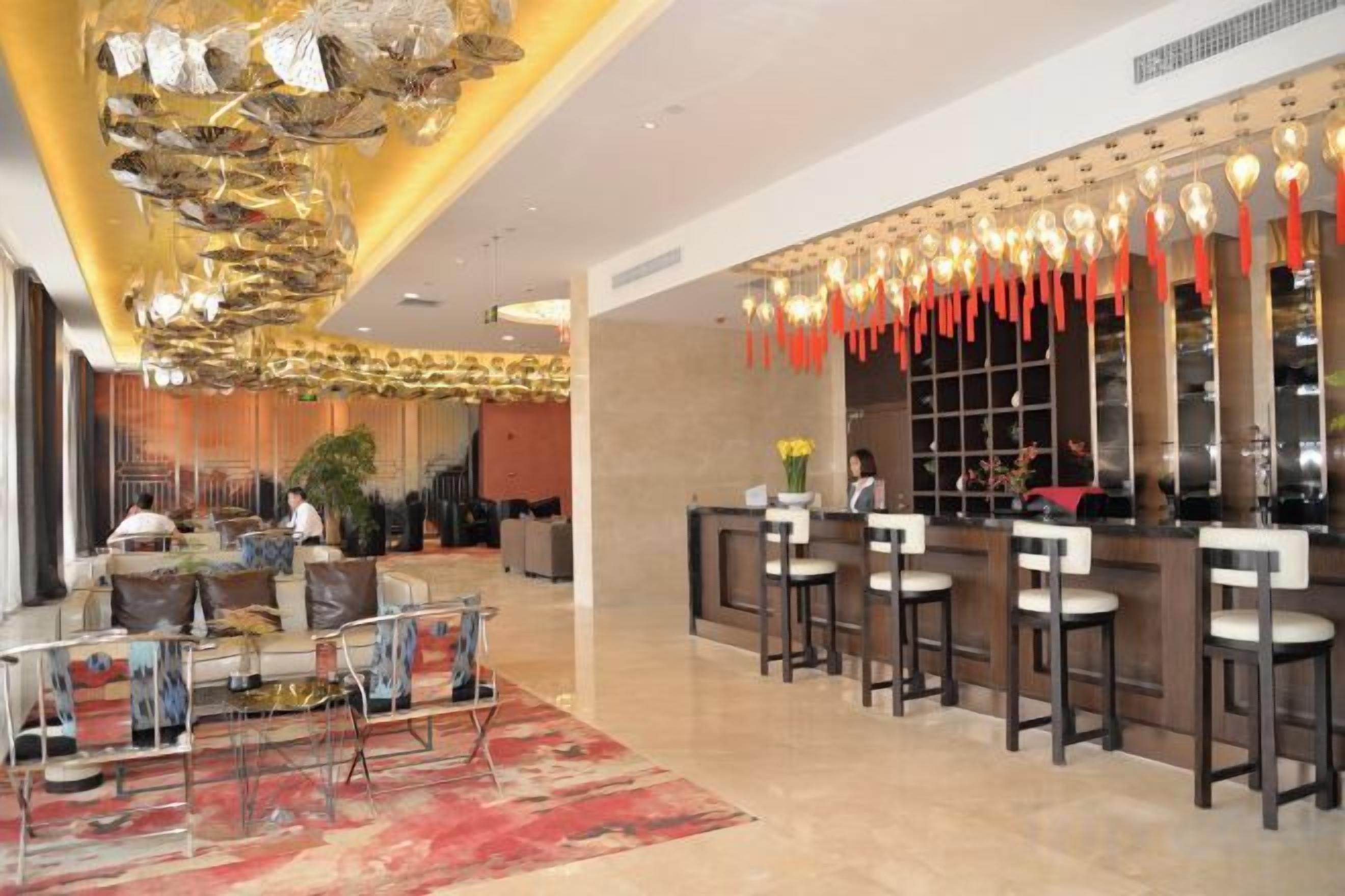 A hotel lobby with a reception desk, bar area, seating, and a decorative ceiling.