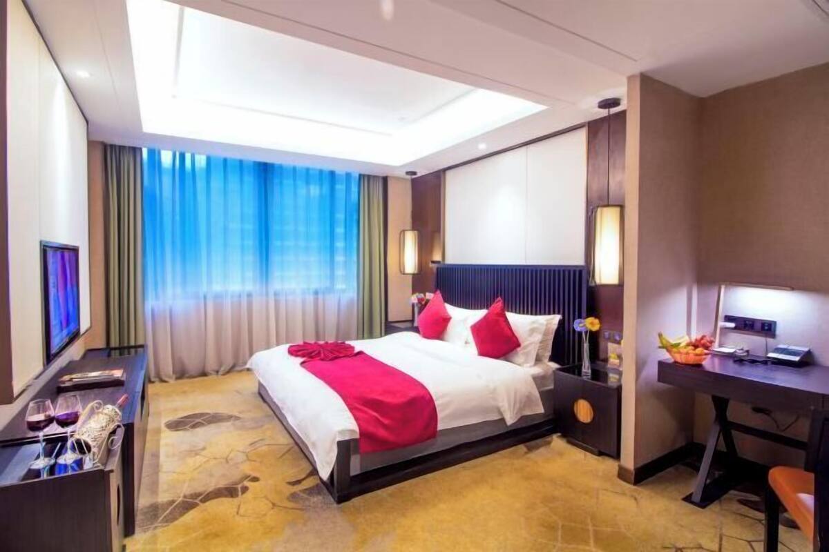 A hotel room with a bed, desk, TV, and curtains.