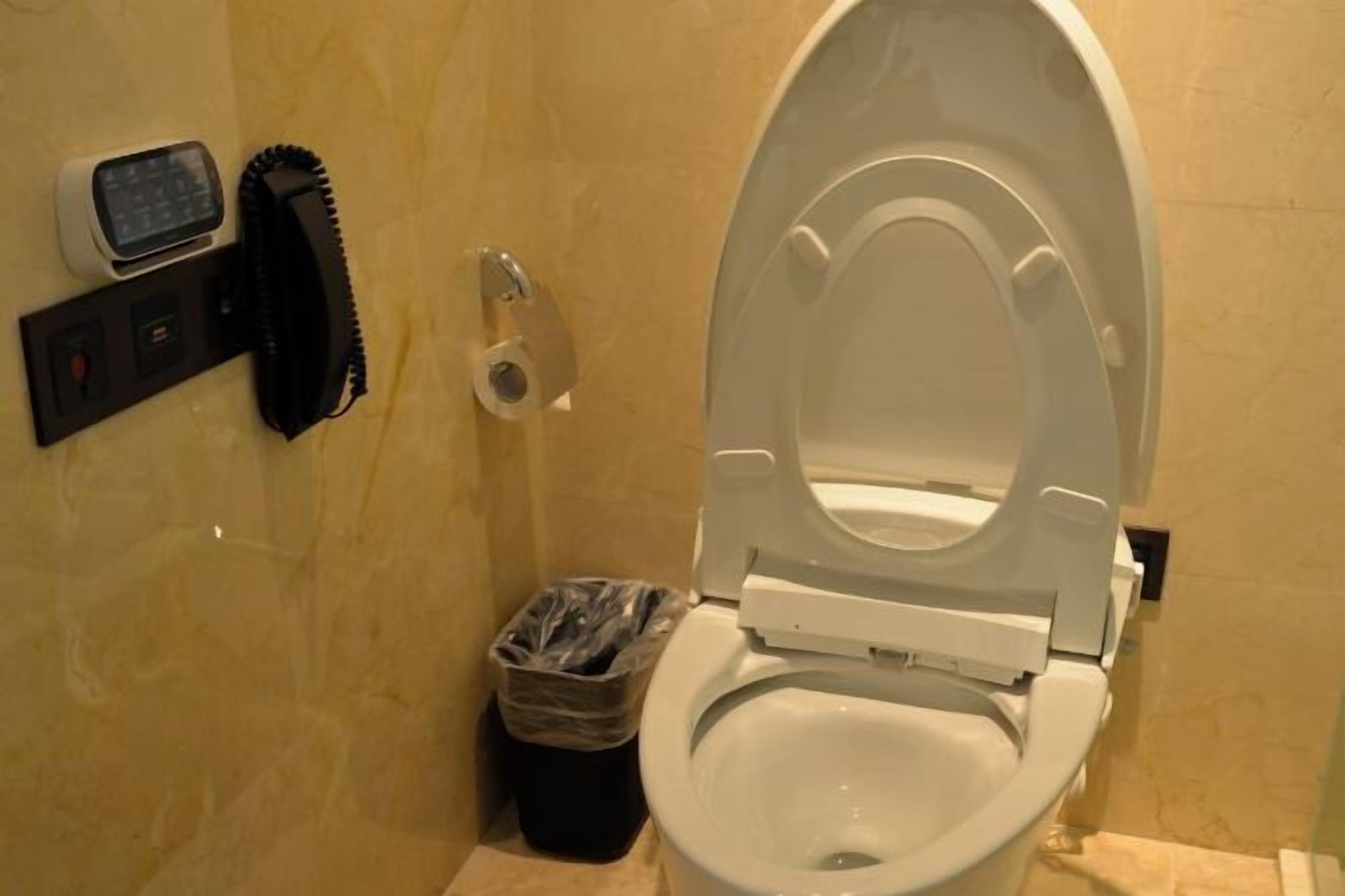 Une salle de bain équipée de toilettes, d’un sèche-mains, d’une poubelle et d’un téléphone fixé au mur.