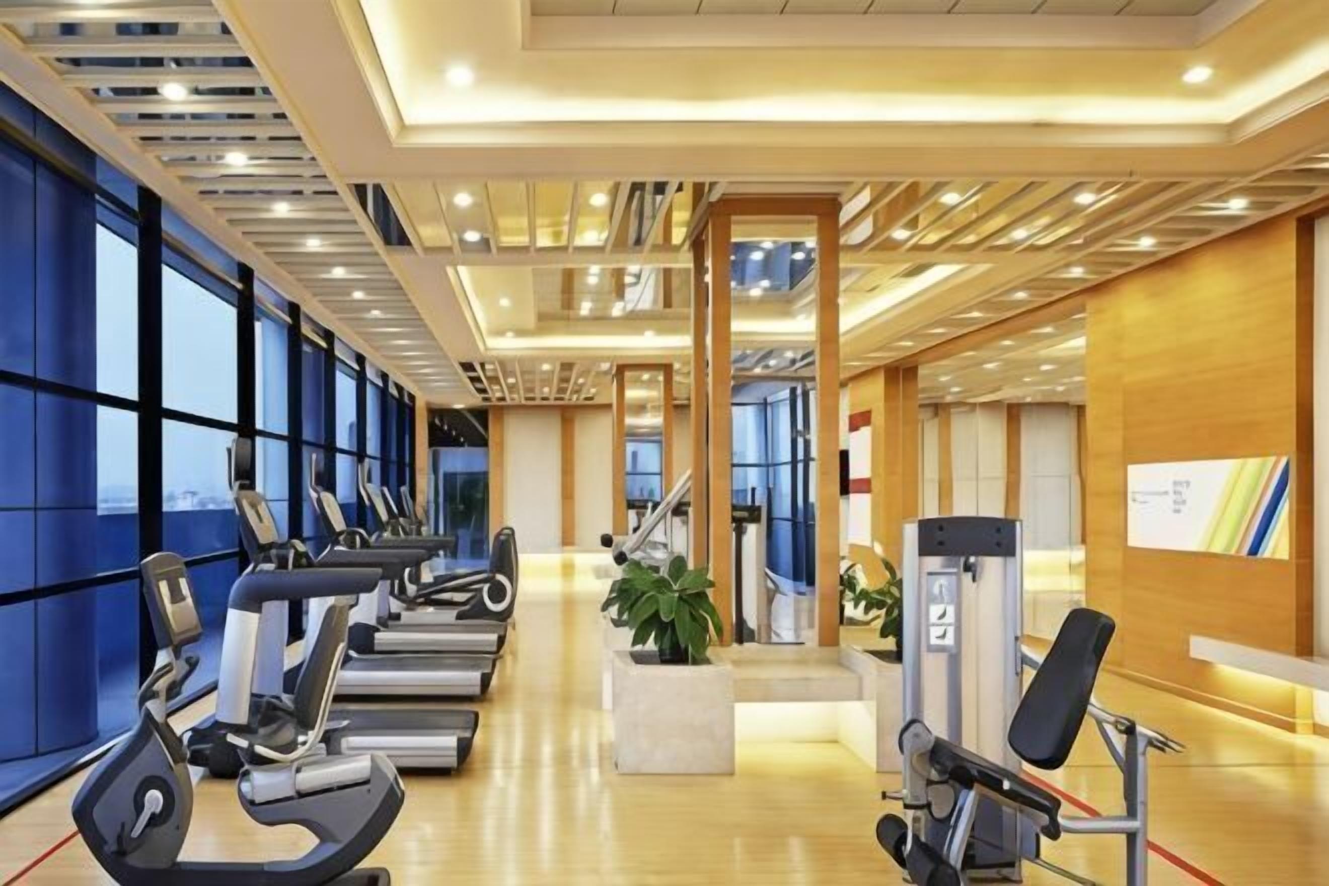 A gym with treadmills, weight machines, and a large windowed wall.