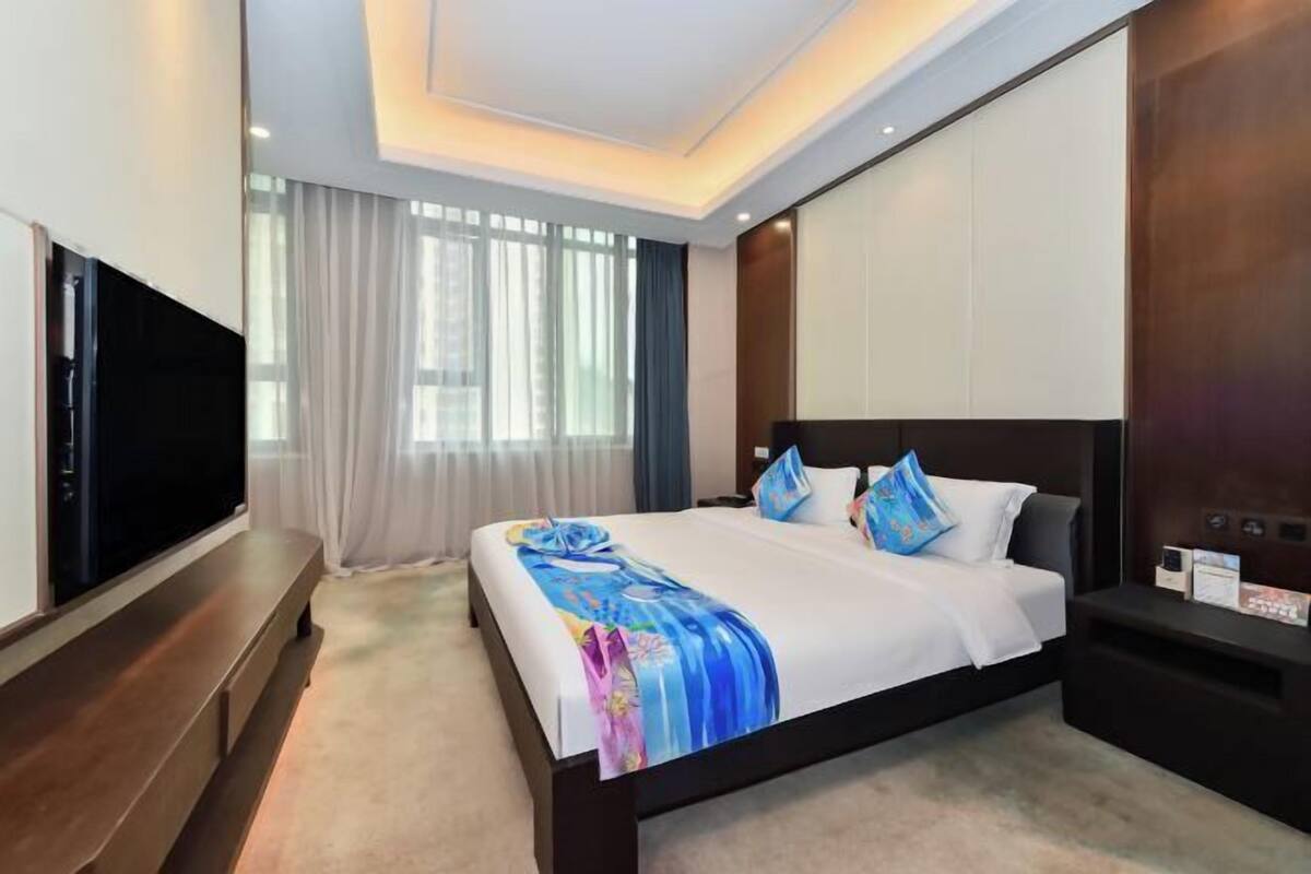A modern hotel room with a large bed, a flat-screen TV, and a wooden bench.