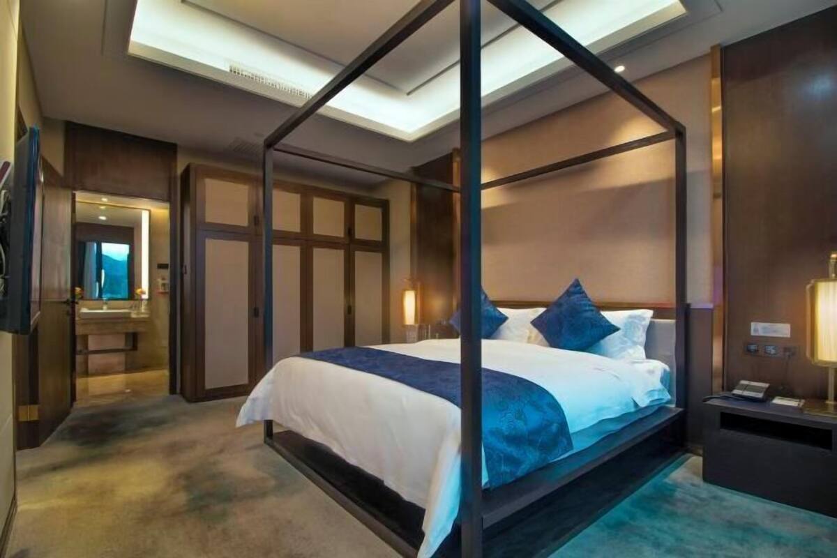 A four-poster bed with a canopy, a bedside table with a lamp, and a view of the room's interior.