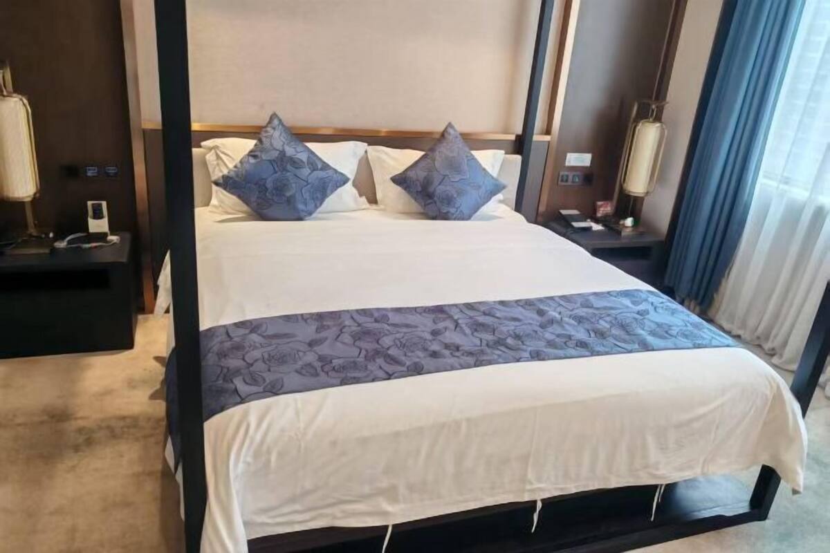 A hotel room with a bed, nightstands, a lamp, and curtains.