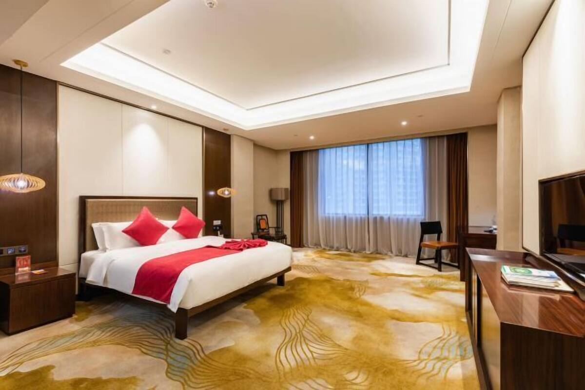 A hotel room with a large bed, a desk, a chair, and a TV.