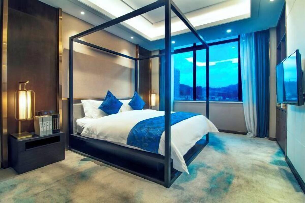 A modern hotel room with a four-poster bed, a city view, and a flat-screen TV.
