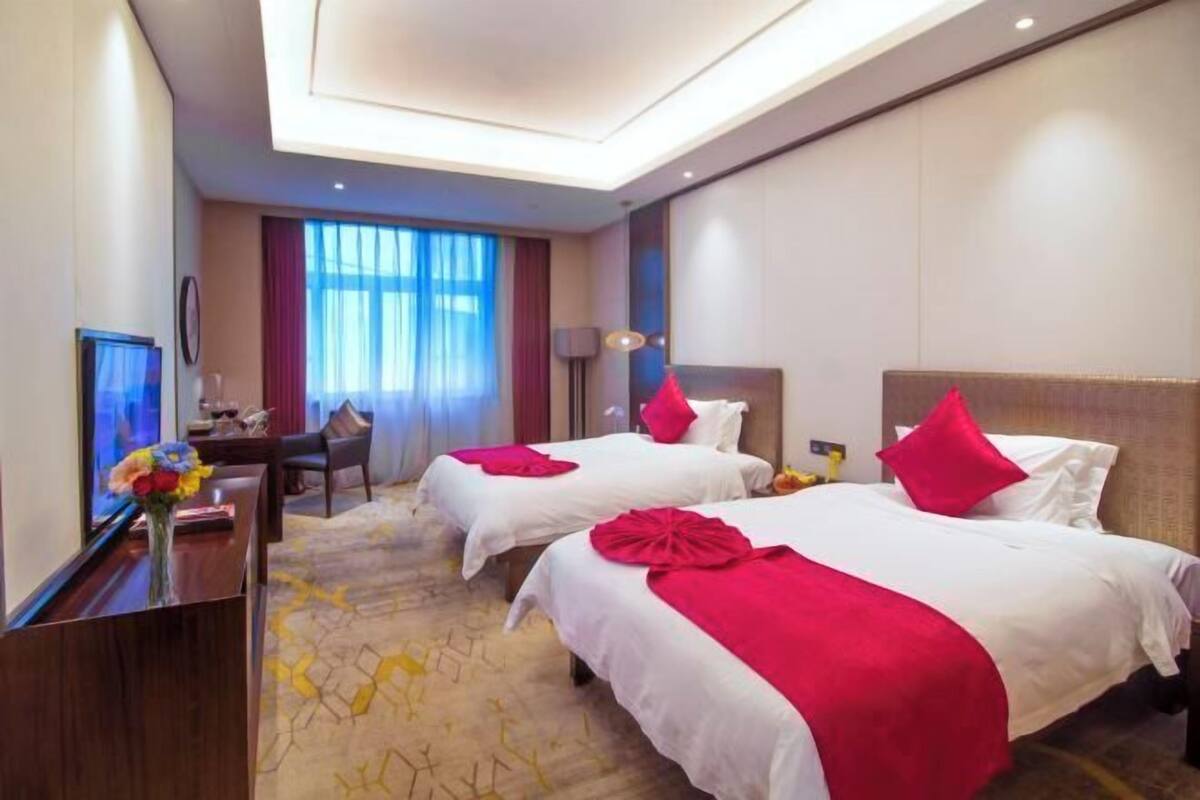 A hotel room with two beds, a desk, a chair, and a television.