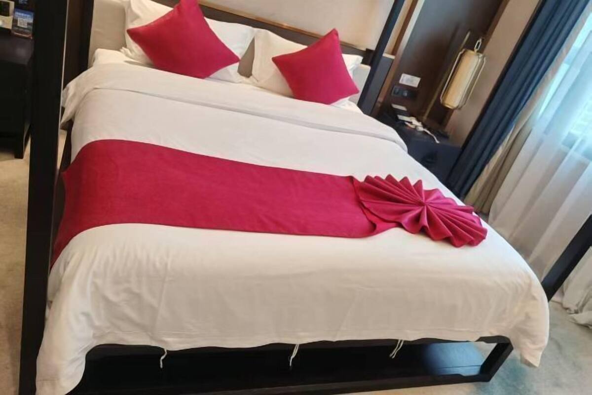 A neatly made bed with white and red bedding, a decorative red pillow, and a black frame.