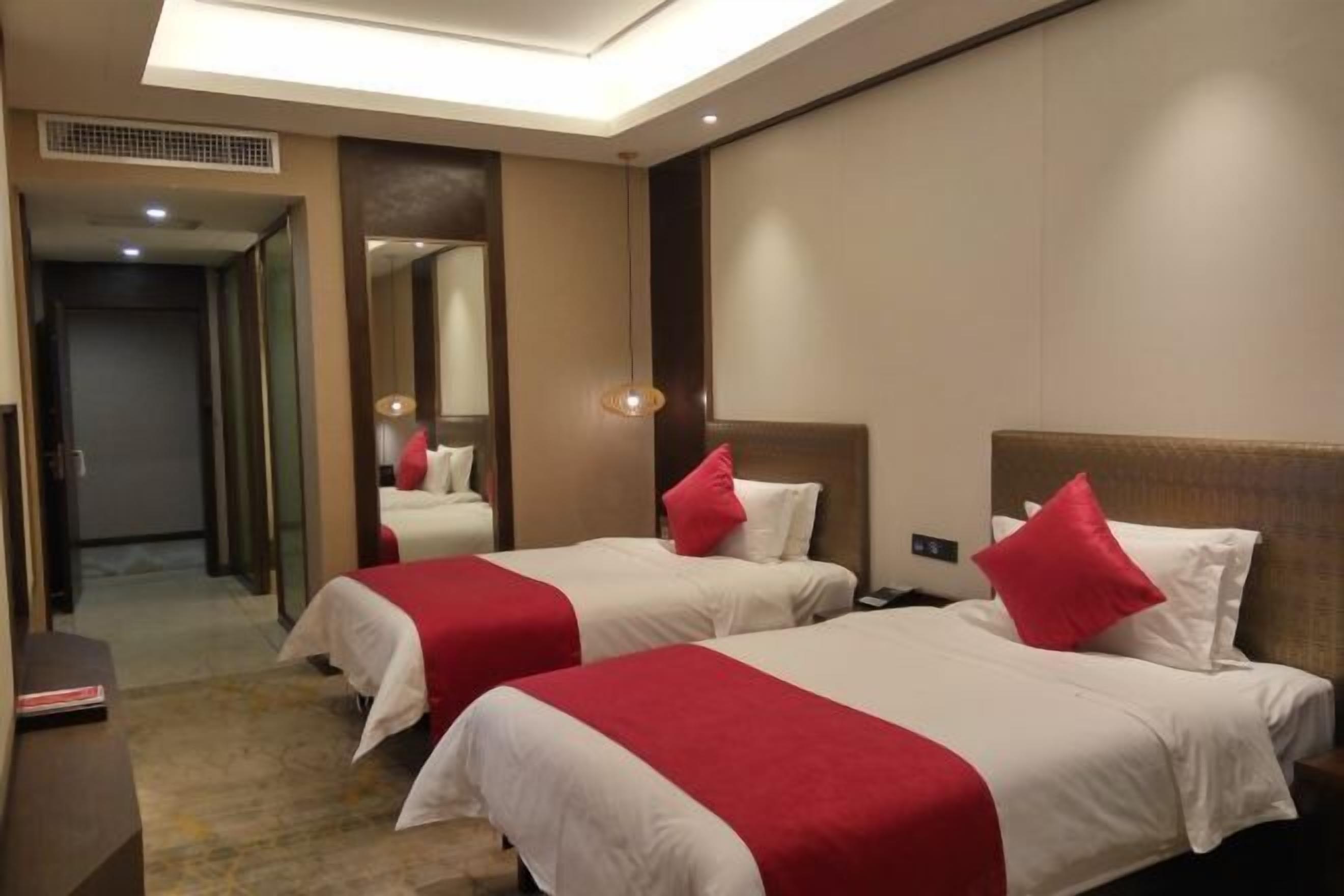 A hotel room with two beds, each with a red and white bedspread, a bedside table, and a mirror on the wall.