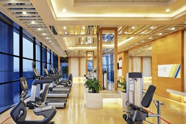 Un gimnasio con máquinas de cardio, banco de pesas y amplios ventanales.