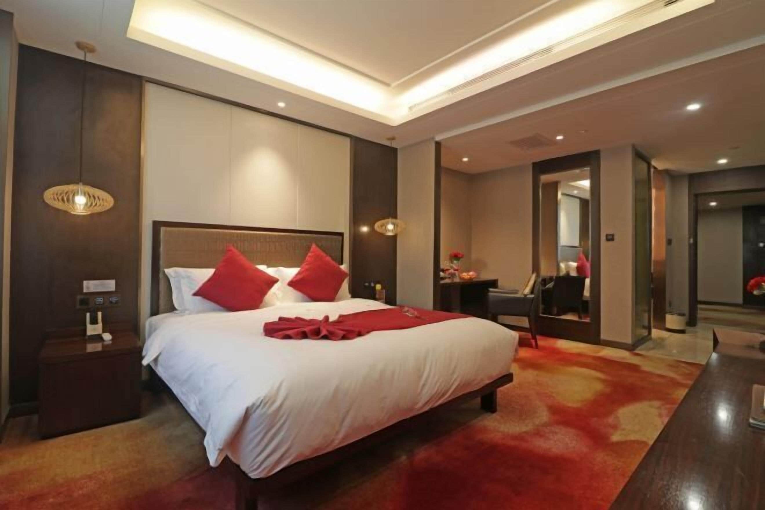 A hotel room with a large bed, a nightstand, a desk, and a mirror.