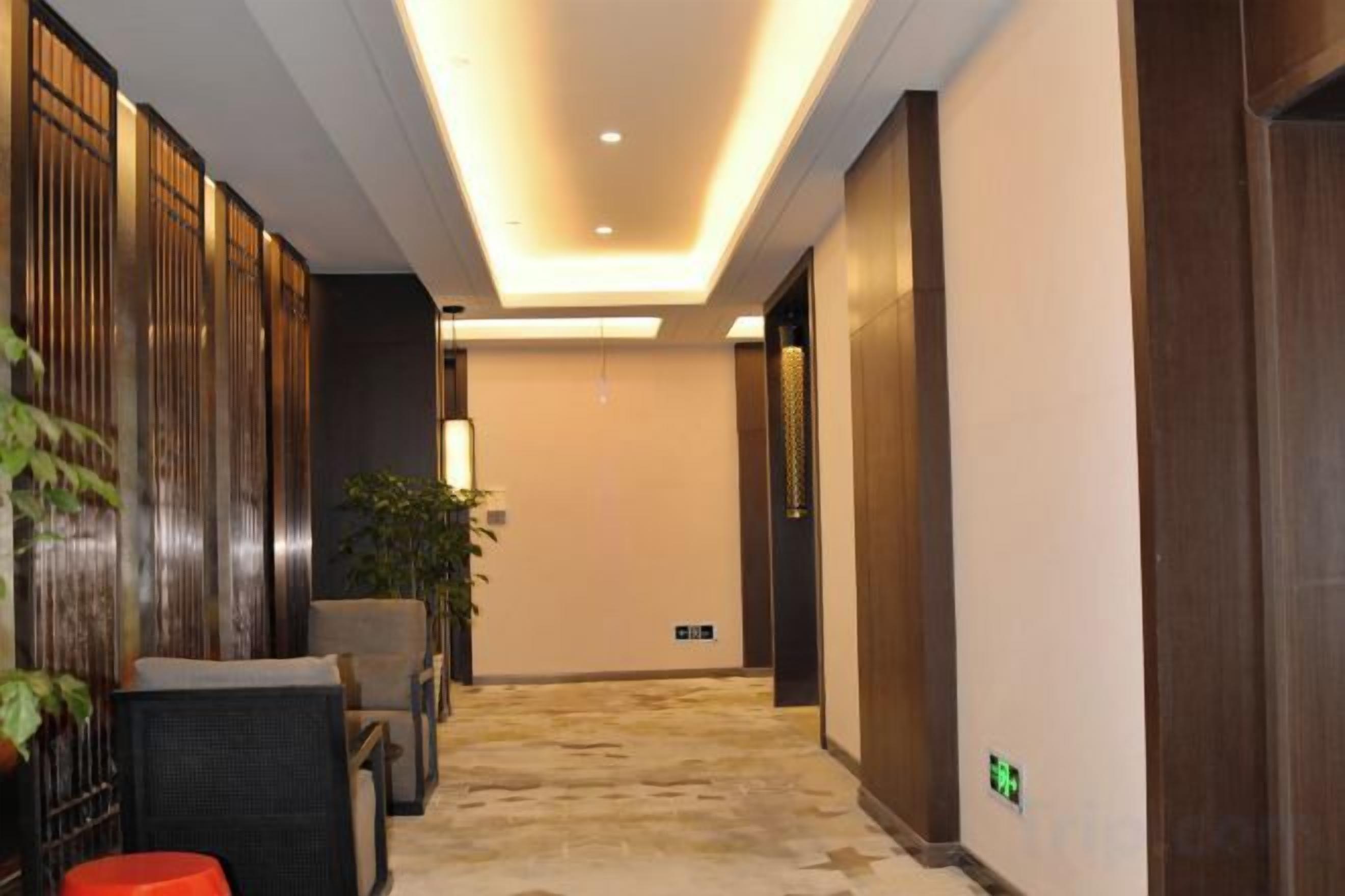 A hotel hallway with a carpeted floor, wooden paneling on the walls, and a reception desk with chairs.