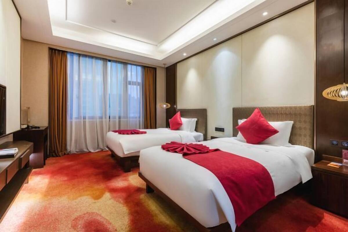 A hotel room with two beds, a large mirror, a TV, and a carpeted floor.