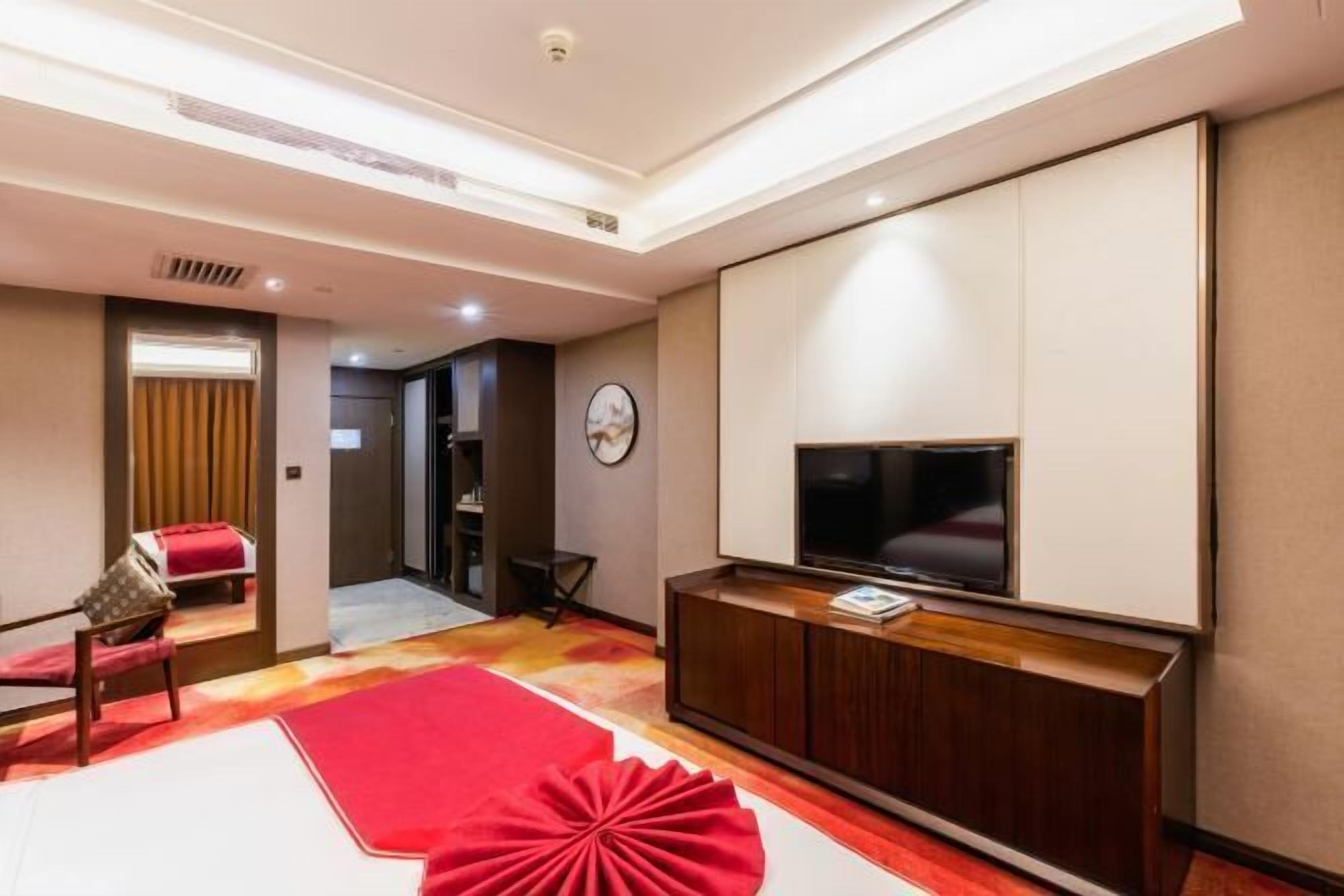 A modern hotel room with a large flat-screen TV, a wooden entertainment unit, and a red accent rug.