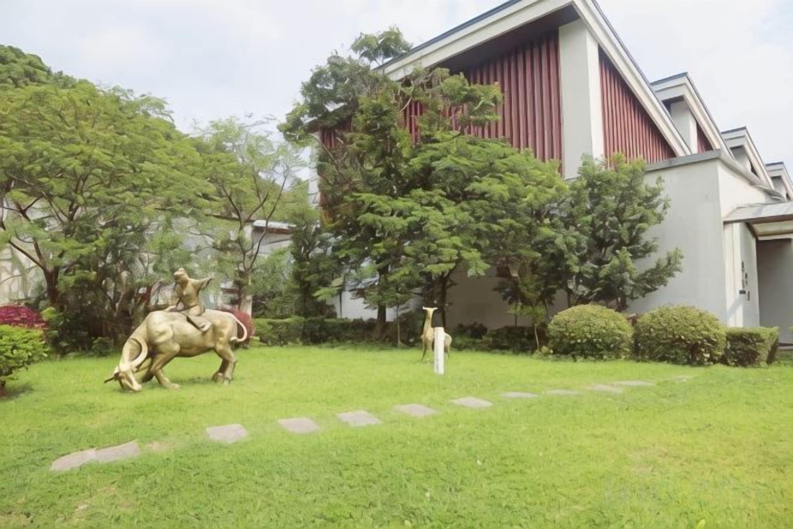 Un edificio con fachada roja y blanca, un césped y una estatua de un jinete a caballo.