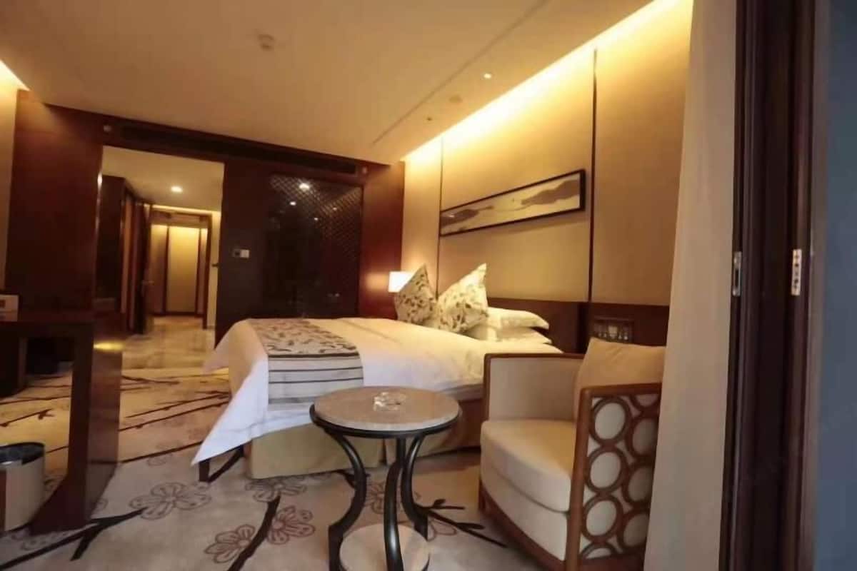 Quarto de hotel com uma cama, uma mesinha redonda, um sofá e um objeto decorativo na parede.