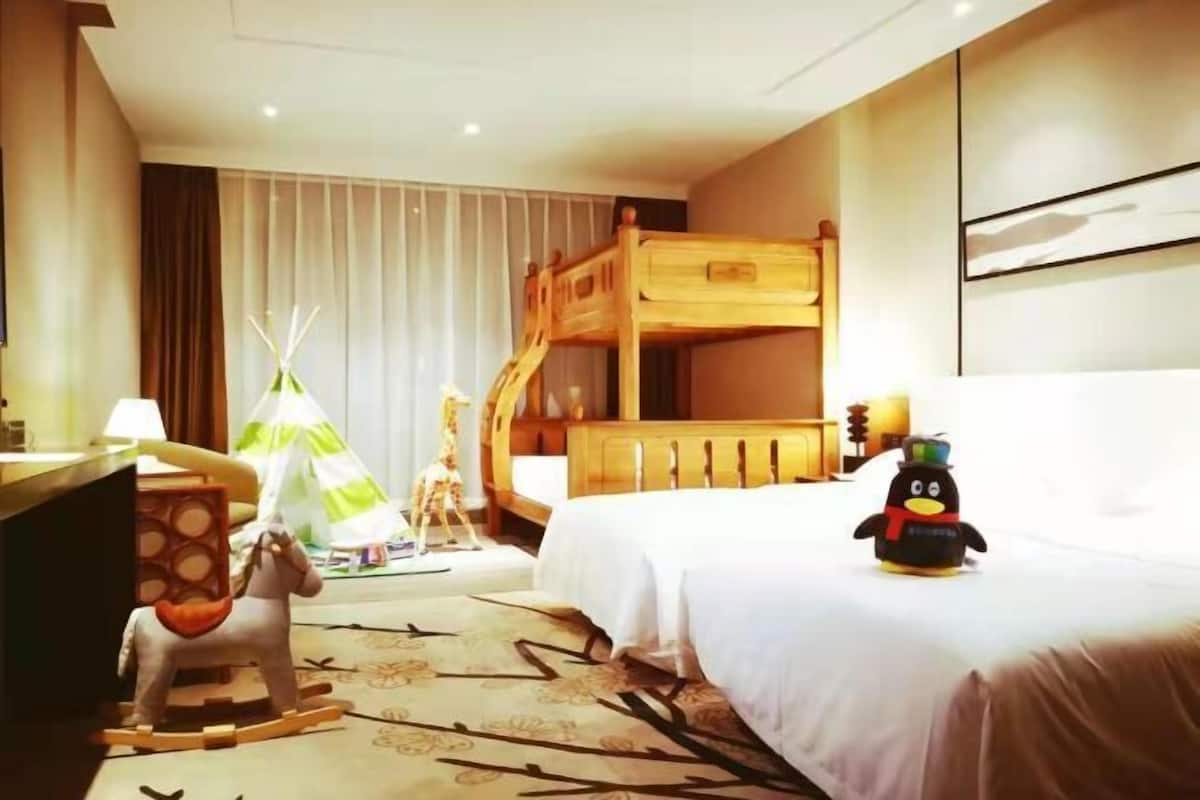 Quarto de hotel com uma cama de beliche, uma escrivaninha com luminária, um cavalinho de balanço, um brinquedo de pinguim e um tipi.