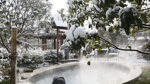 A circular hot tub surrounded by snow-covered plants and a wooden structure. - Chuishan Hot Spring Resort (Zhenjiang)