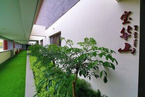 A corridor with a green artificial turf, a wall with a red sign, and a row of green plants. - Chuishan Hot Spring Resort (Zhenjiang)