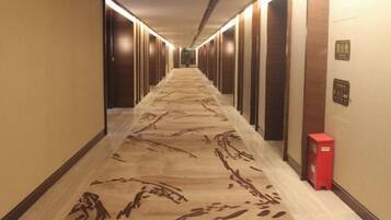 A hotel corridor with a patterned carpet, doors on both sides, and a red object on the right wall.
