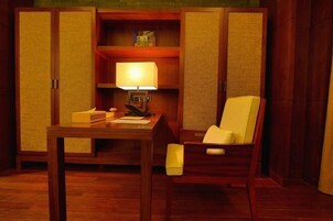 Una habitación con un escritorio de madera, una silla, una lámpara y una estantería con libros y una caja.