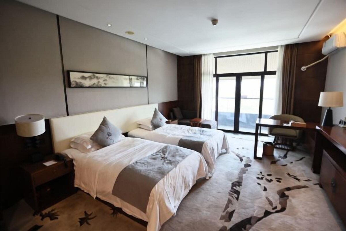 A hotel room with two beds, a desk, a chair, and a large window.
