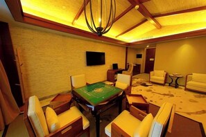 A room with a green felt table, four chairs, a television on the wall, and a carpet with a cow print design.