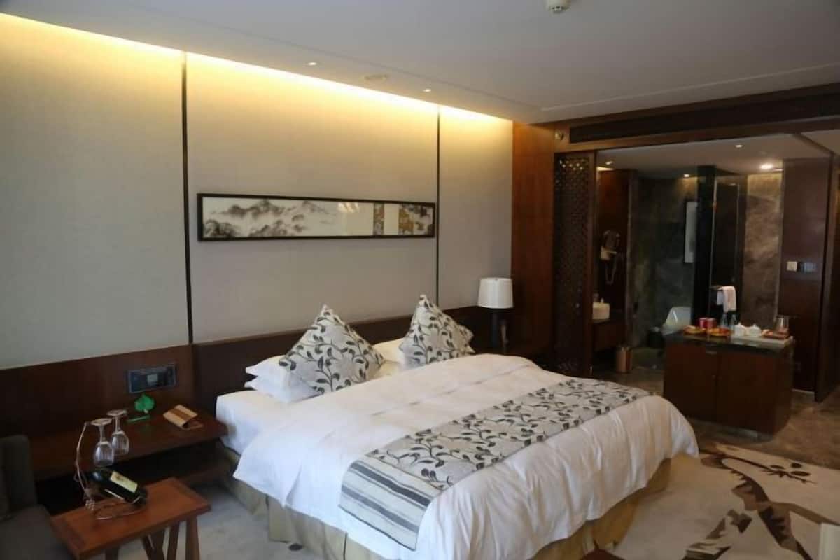 Quarto de hotel com cama, mesa de cabeceira, abajur e um quadro na parede.