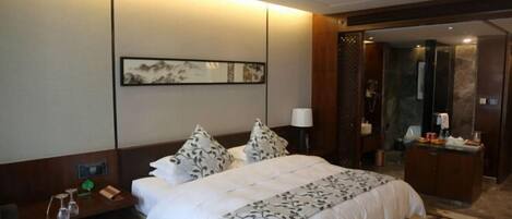 A hotel room with a bed, bedside table, lamp, and a painting on the wall.