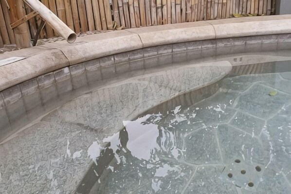 A pool with a curved edge and a bamboo fence in the background.