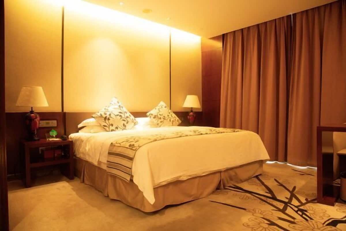 Quarto de hotel com uma cama, duas luminárias de cabeceira, um criado-mudo e um espelho.