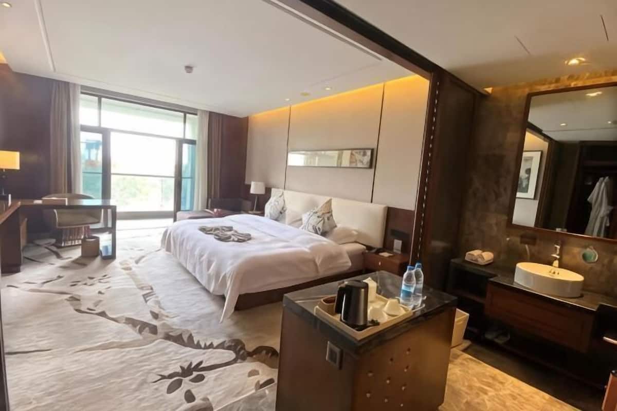 Quarto de hotel com uma cama grande, uma escrivaninha, toucador com espelho e banheiro.