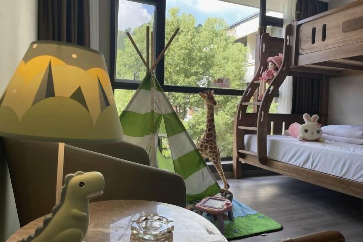 A room with a bunk bed, a green tent, a giraffe decoration, a lamp, and a dinosaur toy.
