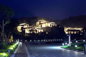 Un bâtiment bien éclairé, à plusieurs niveaux, entouré d’une zone pavée et agrémentée de luminaires.
