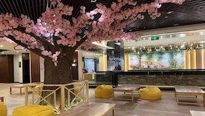 A modern interior with wooden benches and yellow bean bags, a large artificial cherry blossom tree, and a bar area with a mural in the background. - Chuishan Hot Spring Resort (Zhenjiang)