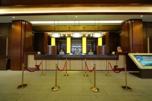 Un espace d’accueil d’hôtel comprenant un comptoir de réception, un écran numérique et une file de potelets.