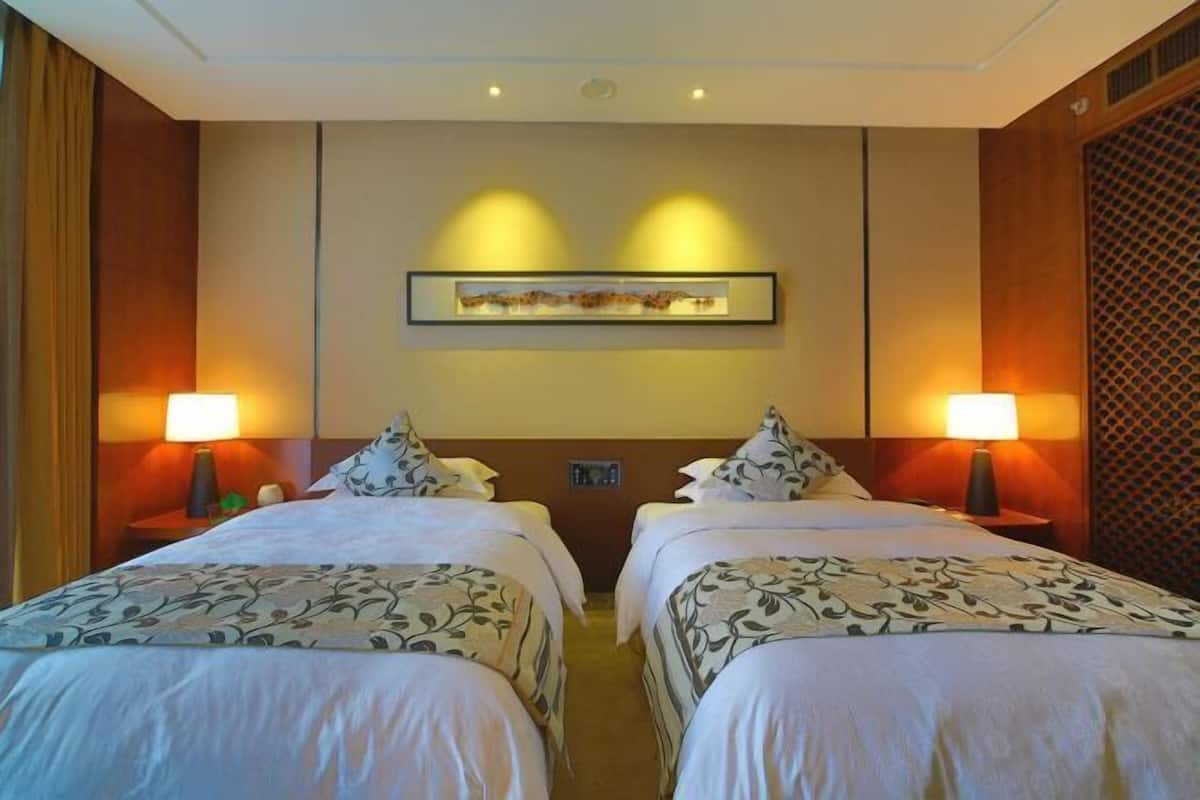 Quarto de hotel com duas camas, uma obra de arte emoldurada acima e duas luminárias de cabeceira.