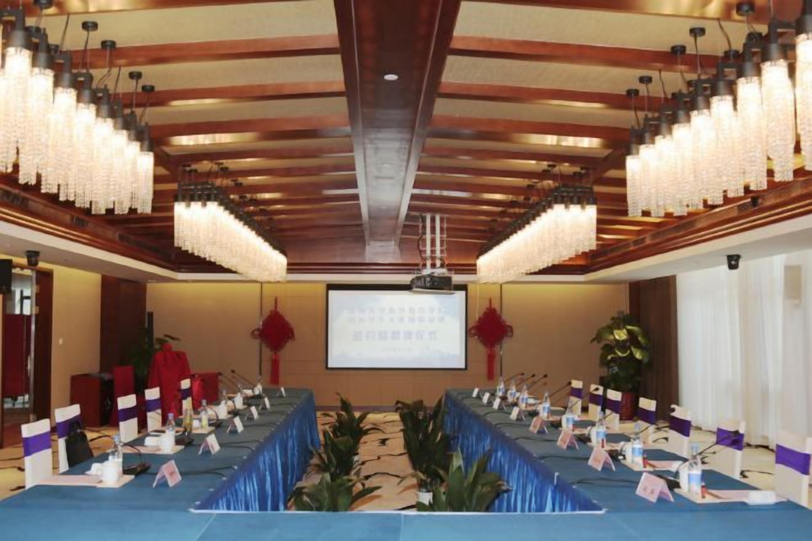 A conference room with a long table, microphones, and a screen at the front.