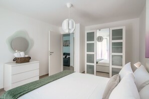 A modern bedroom with a bed, a dresser, a mirror, and a wardrobe with frosted glass doors.