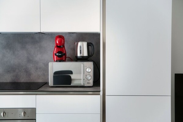 A kitchen with a microwave, a red coffee maker, and a stainless steel kettle on the countertop.