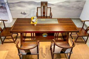 Une table de salle à manger rectangulaire en bois, accompagnée de six chaises, d’un élément décoratif central et d’une fresque murale.