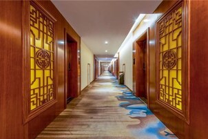 A long, narrow hallway with wooden doors featuring intricate geometric patterns and a carpet with a blue and brown design.