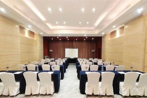 A conference room with rows of tables and chairs, a projector screen, and a podium. - Basu Nujiang Yun Hotel (Basu)