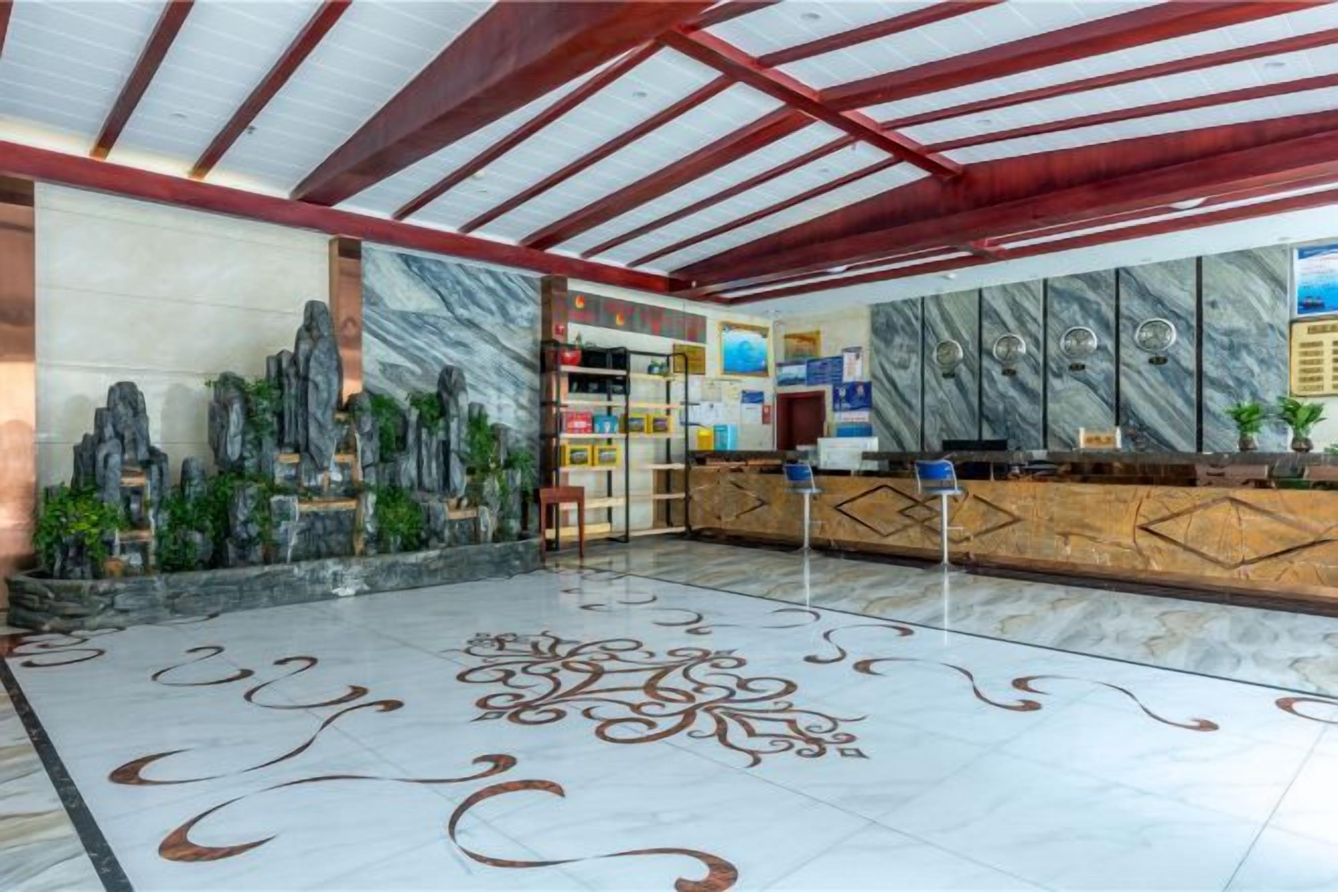 Zona de recepción con suelo de mármol, mostrador de recepción, pared con jardín de rocas y techo con vigas de madera.