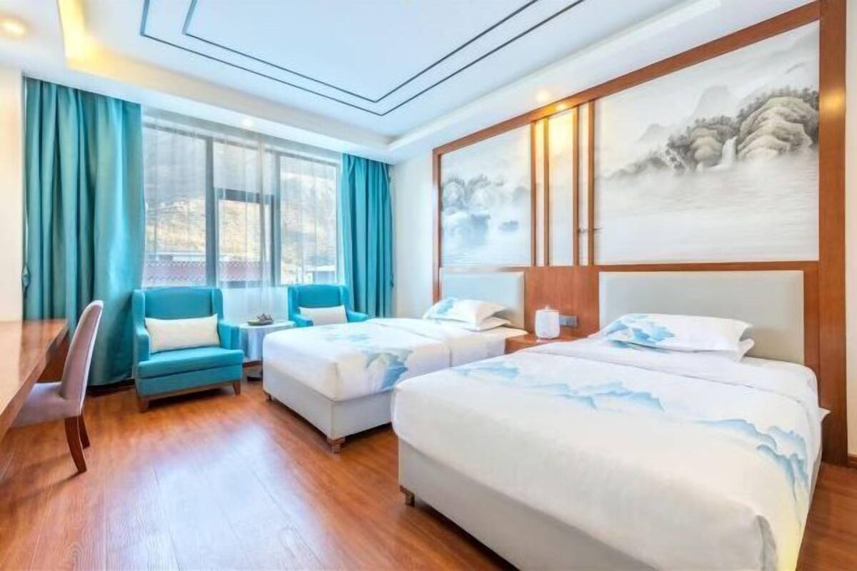 A hotel room with two beds, a desk, a chair, and a large painting on the wall.