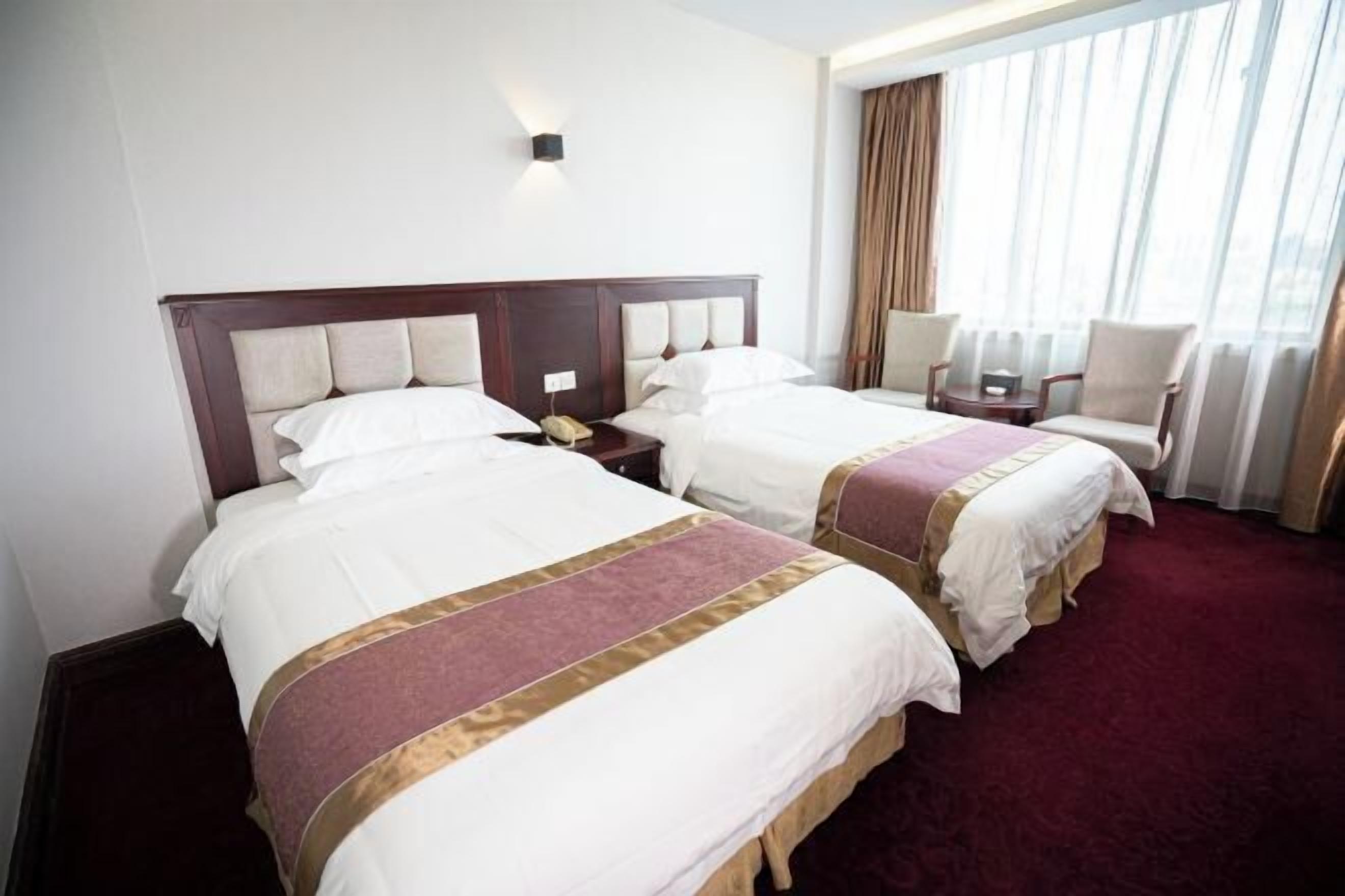 A hotel room with two beds, a nightstand, a chair, and a large window with curtains.
