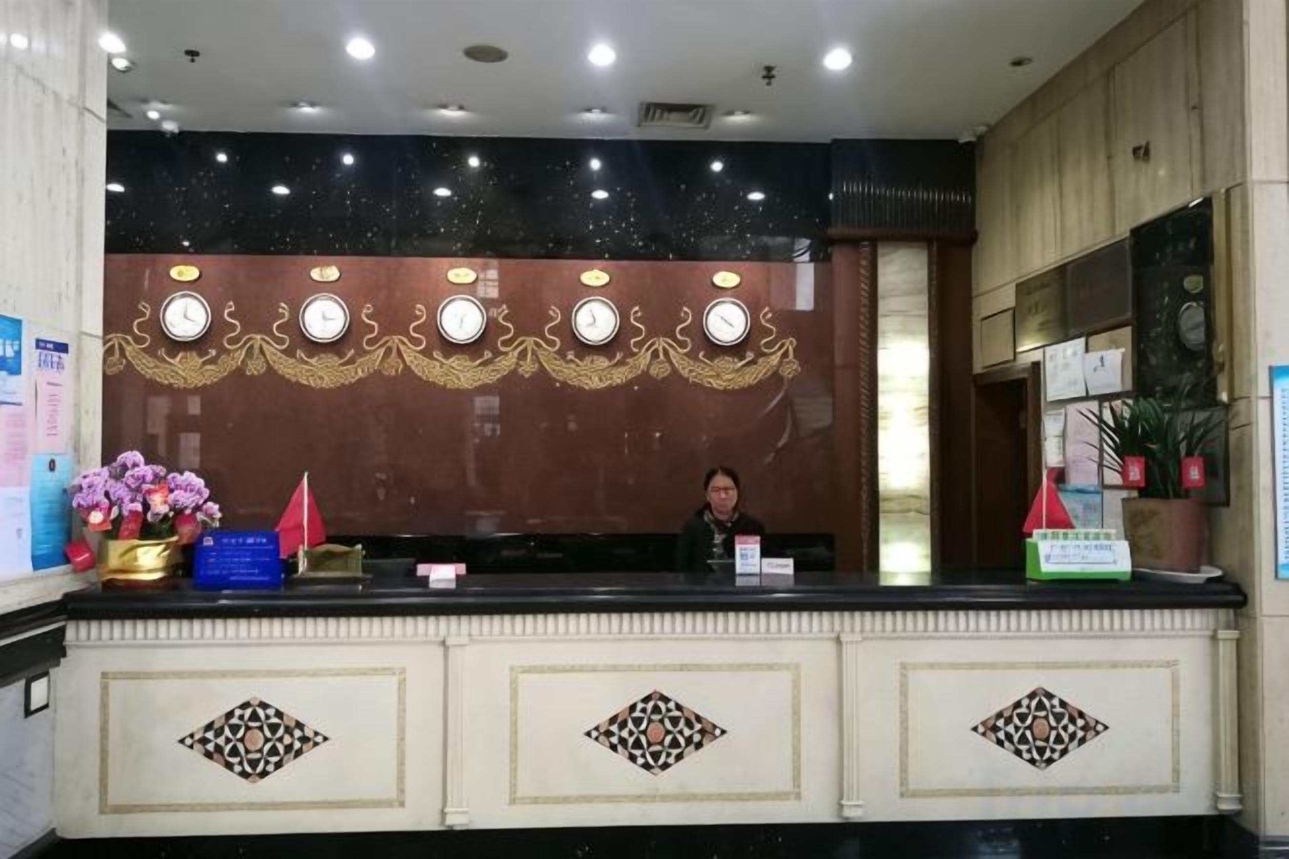 A reception desk with a person seated behind it, a decorative wall with circular patterns, and a potted plant to the right.